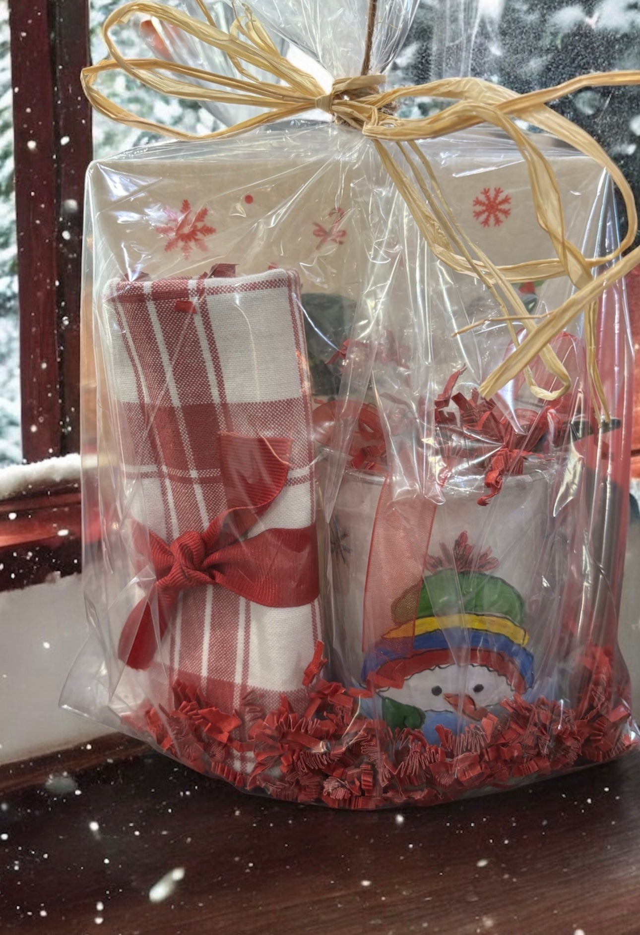 Gift set wrapped in clear cellophane with decorative ribbons, placed on a surface with a snowy outdoor background.