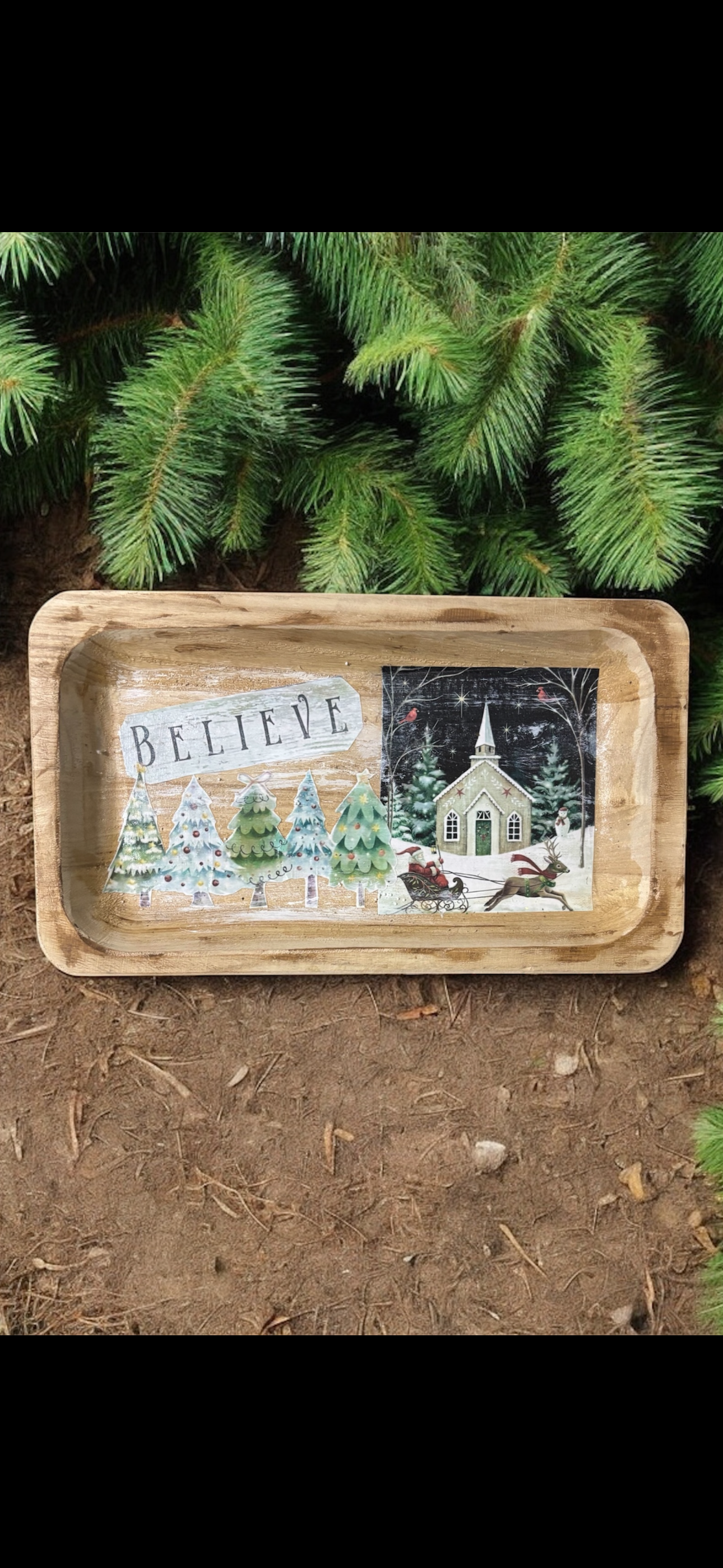 Decorative tray with Christmas scene and 'BELIEVE' text, placed on a natural surface with greenery.